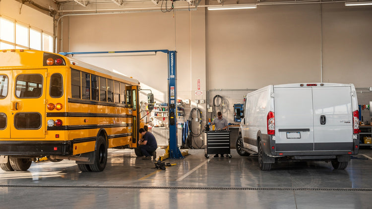 Yellow school bus and white cargo van safely on the floor in a commercial fleet service shop
