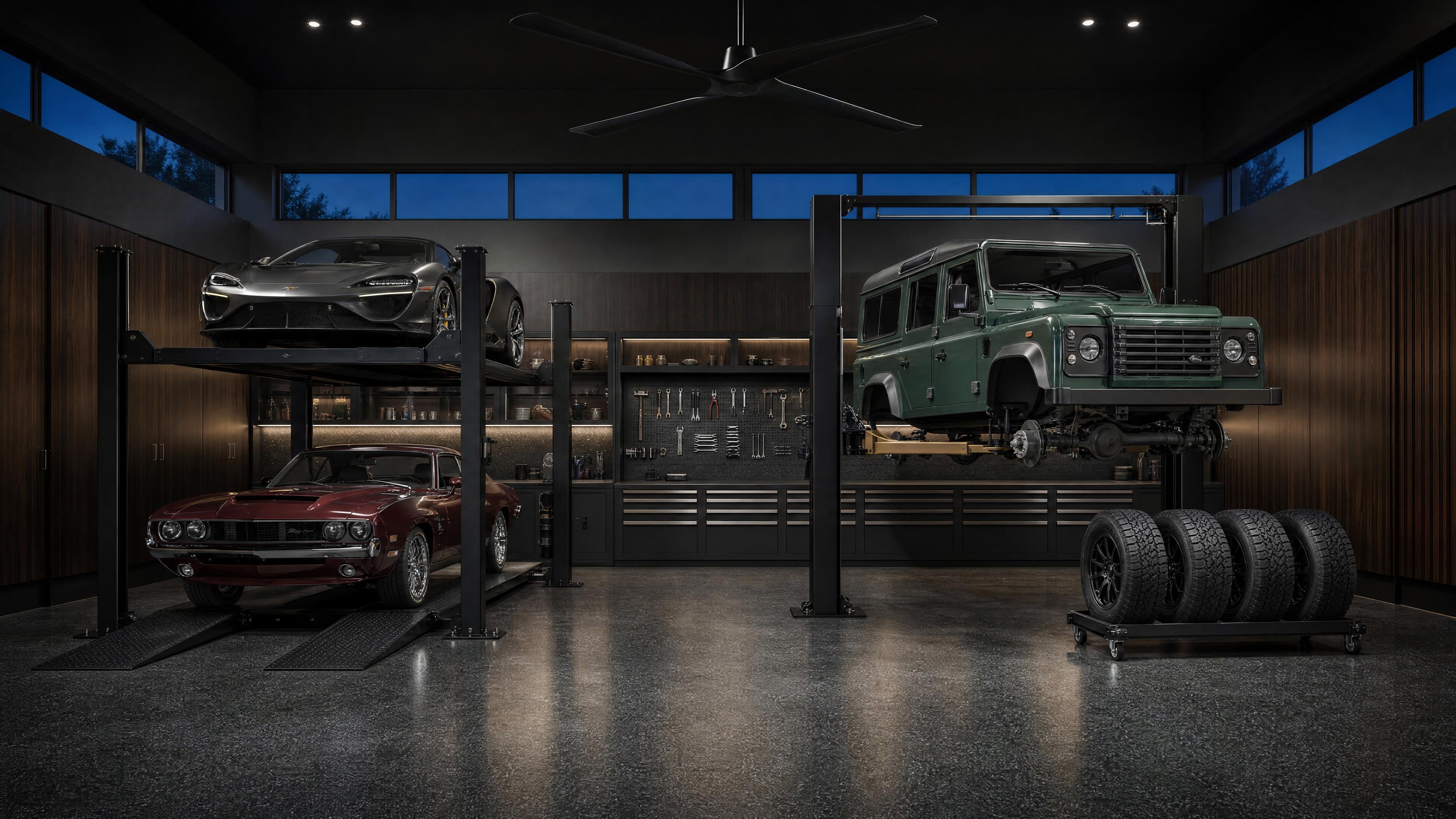 Luxury residential Dream Garage with a Challenger four-post parking lift, a black Challenger two-post lift, three collector vehicles and an industrial ceiling fan